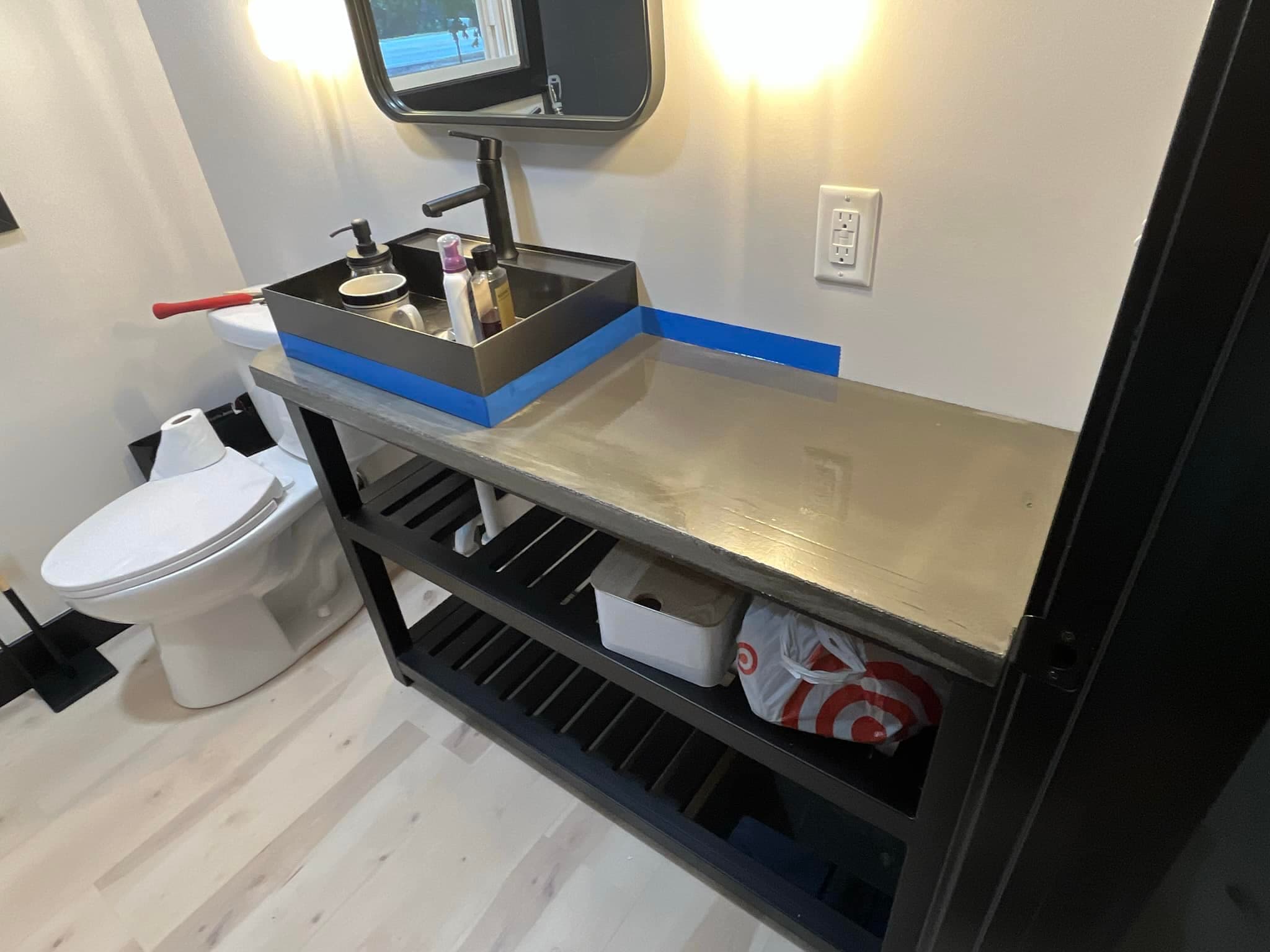 Modern bathroom with a concrete countertop, black sink, and organized shelves beneath.