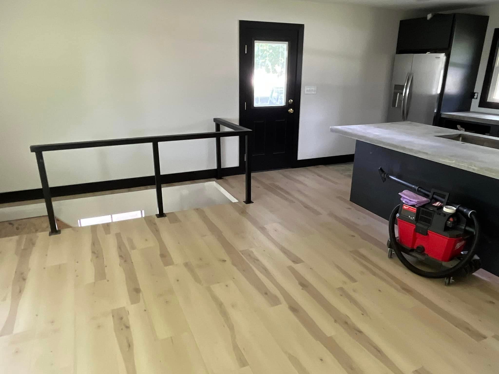 Modern kitchen interior featuring light wood flooring, black accents, and a vacuum cleaner.